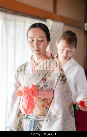 Une femme en kimono est aidée par une autre femme. La femme dans le kimono porte un arc rouge Banque D'Images