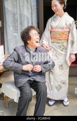 Une femme en kimono sourit à une femme plus âgée. La femme âgée est assise sur une chaise Banque D'Images