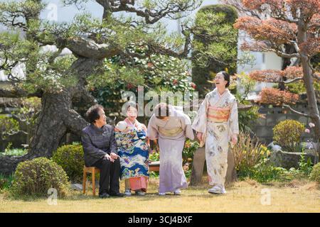Quatre femmes vêtues de vêtements japonais traditionnels rient et se tiennent debout dans un jardin. La scène est légère et joyeuse Banque D'Images
