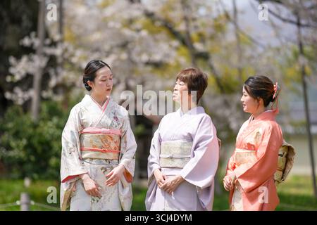 Trois femmes vêtues de vêtements japonais traditionnels se tiennent debout dans un parc, se regardant. Scène est amicale et détendue, comme les femmes semblent être enj Banque D'Images