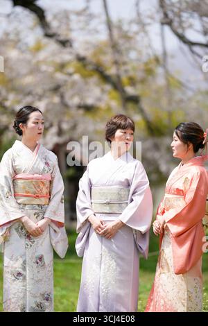 Trois femmes vêtues de vêtements traditionnels japonais se tiennent debout dans un parc. Ils sourient et se regardent Banque D'Images