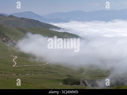 Un paysage montagneux à couper le souffle avec des collines verdoyantes, des chemins de terre sinueux et des nuages épais dérivant à travers les vallées. La brume crée un rêve Banque D'Images