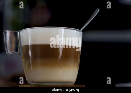 Latte macchiato dans une tasse en verre avec une cuillère posée sur la mousse, montrant les différentes couches d'espresso, de lait et de mousse Banque D'Images
