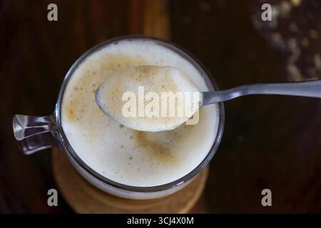 Mousse de café crémeuse soulevée par une cuillère d'une tasse en verre, créant une vue rapprochée de la texture riche et des bulles mousseuses Banque D'Images