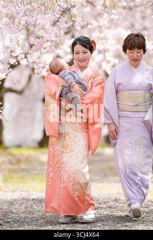Une femme tient un bébé tout en portant un kimono. Elle marche avec deux autres femmes Banque D'Images
