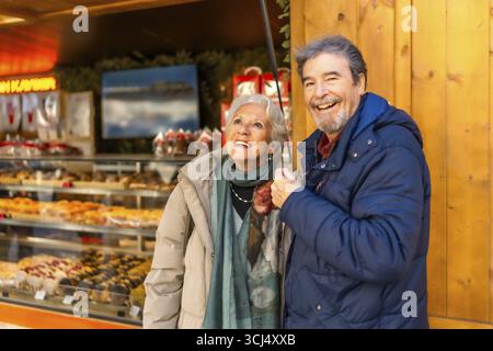Joyeux couple senior profitant du marché de noël, du shopping et s'amusant pendant les vacances d'hiver Banque D'Images