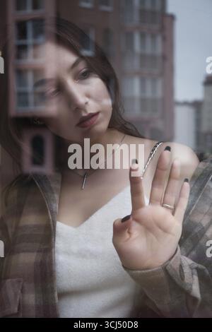 Triste jeune femme solitaire regardant par la fenêtre la ville moderne Banque D'Images