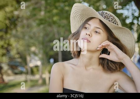 Mignonne jeune femme à la rue ensoleillée assis, regardant de côté, gros plan portrait Banque D'Images