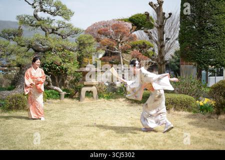 Deux femmes en kimonos jouent au badminton dans un parc. L'une des femmes tient un ventilateur, qu'elle utilise pour bloquer la balle de son oppon Banque D'Images