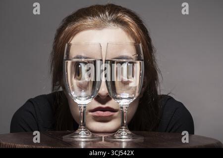 Fille regarde la caméra à travers des verres à vin avec l'image tonique de l'eau Banque D'Images
