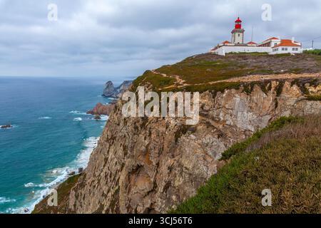 Une vue panoramique sur un phare et un groupe de bâtiments perchés sur une falaise accidentée surplombant le vaste océan turquoise sous un ciel nuageux Banque D'Images