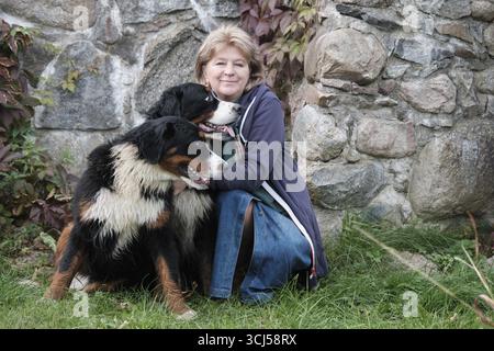 Femme avec deux chiens de montagne bernois près du mur de pierre regardant la caméra Banque D'Images