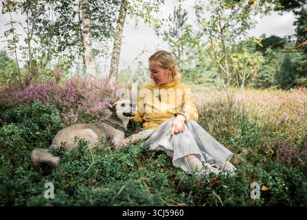 Femme avec chien se relaxant dans la prairie forestière fleurie Banque D'Images