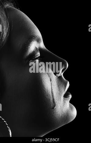 Femme triste avec les yeux fermés pleurant, sur fond noir, gros plan portrait, vue de profil, monochrome Banque D'Images