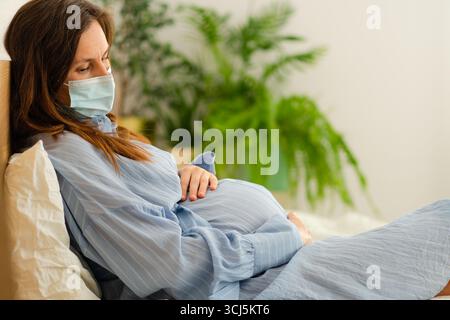 Future mère portant un masque de protection au repos au lit. Gérer les symptômes de la maladie de manière responsable pendant la grossesse. Banque D'Images
