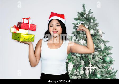 Équipez une jeune athlète féminine debout devant un arbre de Noël avec de l'équipement de gymnastique et des cadeaux, célébrant la saison des fêtes tout en mettant en valeur la force Banque D'Images