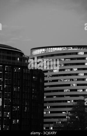 Photographie en noir et blanc de l'architecture moderne londonienne, avec une tour incurvée et une structure adjacente à la façade vitrée. Banque D'Images