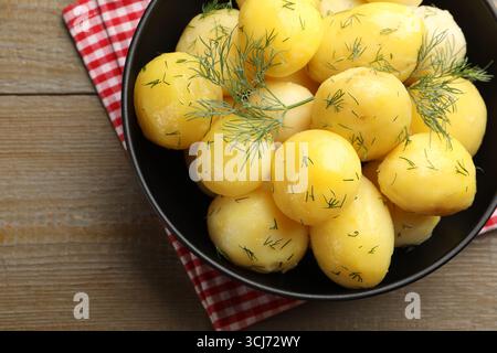 Savoureuses jeunes pommes de terre bouillies avec de l'aneth et de l'huile dans un bol sur une table en bois, vue de dessus Banque D'Images