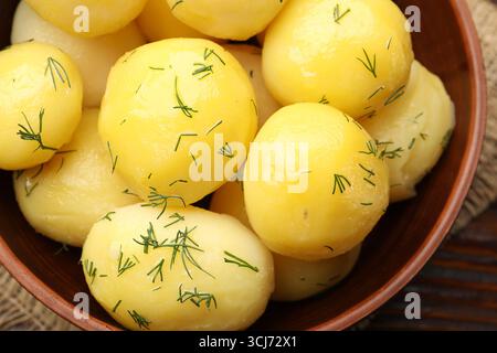Savoureuses jeunes pommes de terre bouillies avec de l'aneth et de l'huile dans un bol sur une table en bois, vue de dessus Banque D'Images