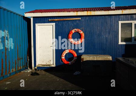 Extérieur bleu du bâtiment avec bouées de sauvetage, porte blanche et lumière du soleil en Islande Banque D'Images