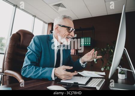 Homme d'affaires senior professionnel s'engageant dans un appel de visioconférence animé dans un environnement de bureau moderne Banque D'Images