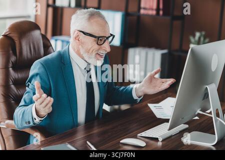 Homme d'affaires mature dans un costume formel s'engageant avec des collègues lors d'une réunion en ligne dans un environnement de bureau moderne Banque D'Images