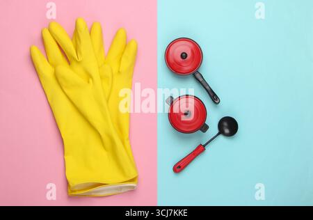 Composition plate de gants de nettoyage, d'outils de cuisine jouet et d'ustensiles sur fond pastel rose bleu. Vue de dessus Banque D'Images