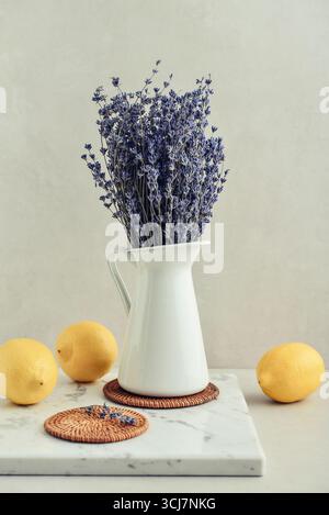 Bouquet de lavande dans une cruche en émail blanc avec des citrons frais sur un fond clair Banque D'Images