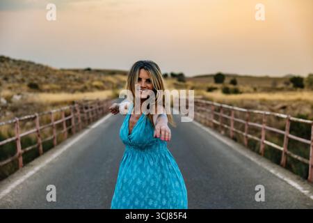 Femme portant une robe bleue jouit de la liberté sur le pont au coucher du soleil Banque D'Images
