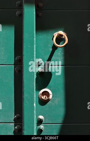 284 bouton de porte en forme d'anneau rouillé et trou de serrure avec plaque d'écusson d'une porte en bois vert cloutée sur la rue via Giovanni Capellini. Porto Venere-Ligurie. Banque D'Images