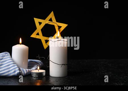 Uniforme de prisonnier, bougies allumées et étoile de David sur fond sombre. Jour du souvenir de l'Holocauste Banque D'Images