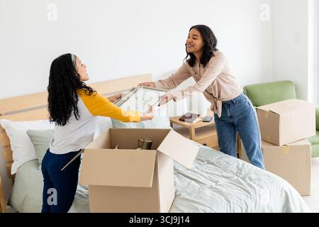 Deux femmes déballant des boîtes sur le lit, souriant et organisant une nouvelle maison ensemble Banque D'Images