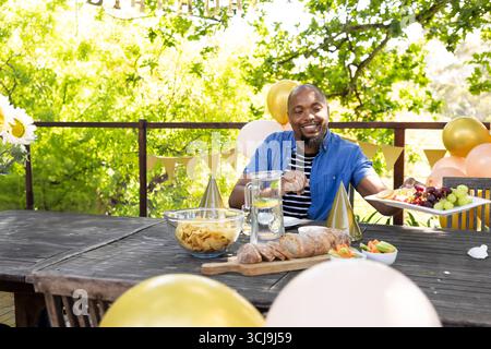Homme afro-américain adulte assis à la table de patio avec des ballons de chips de pichet d'eau citron Banque D'Images