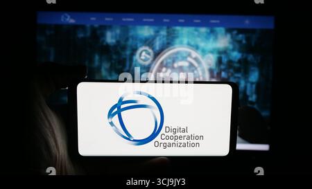 Dans cette illustration photo, une personne tient un téléphone portable avec le logo de Digital Cooperation Organization (DCO) sur l'écran en face de la page Web. Banque D'Images