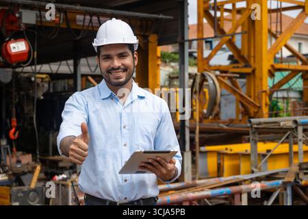 Portrait hispanique ingénieur de construction indien ouvrier masculin sur le chantier de construction avec casque de sécurité et tablette informatique heureux souriant pouces vers le haut Banque D'Images