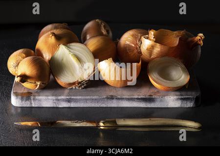 Oignons végétaux sur dalle de pierre avec couteau au premier plan Banque D'Images
