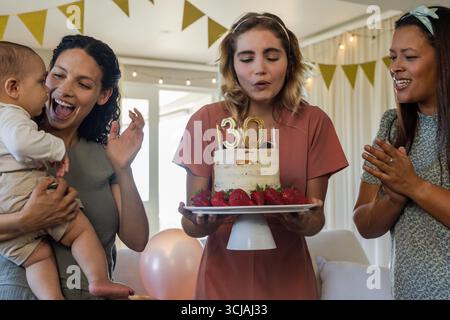Souffler des bougies, femme célébrant 30 ans avec des amis et la famille Banque D'Images