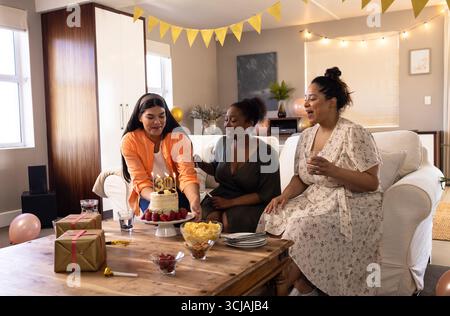 Célébrant l'anniversaire, diverses femmes appréciant le gâteau et les boissons dans le salon confortable Banque D'Images