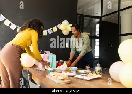 Collègues préparant une table de fête avec des collations et des cadeaux dans un bureau moderne Banque D'Images