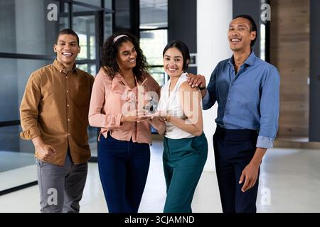 Équipe d'affaires diversifiée au bureau riant et tenant le smartphone ensemble Banque D'Images