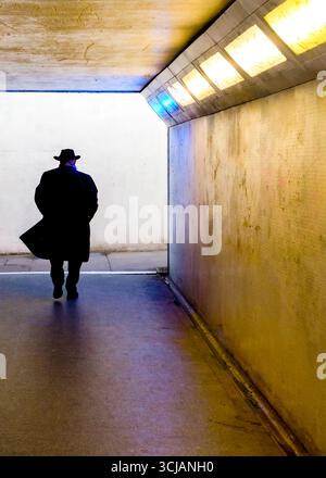 Une personne portant un chapeau et un manteau traverse un tunnel. Banque D'Images