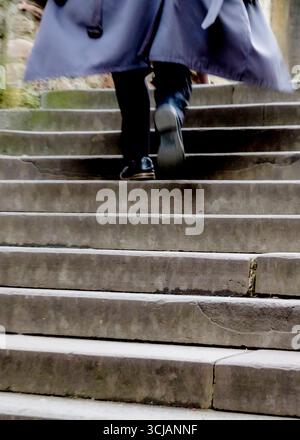 Une personne monte un ensemble d'escaliers en pierre, portant un long manteau. Banque D'Images