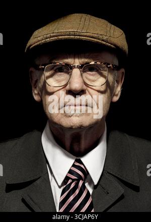 Portrait d'un homme plus âgé portant une casquette en tweed, des lunettes, une veste de costume et une cravate rayée. Banque D'Images