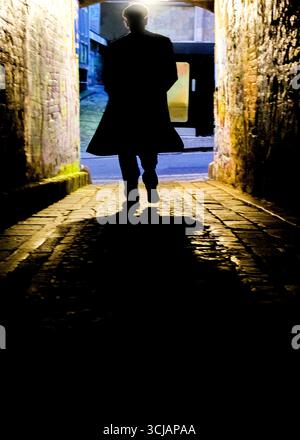 Une silhouette se promène dans une ruelle faiblement éclairée. Banque D'Images