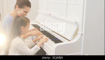 Mère guidant la fille jouant les touches sur le banc par piano droit blanc à la maison avec fenêtre multi-vitrage Banque D'Images