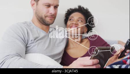 Couple assis sur le canapé dans le salon, tenant tablette et smartphone avec superposition de réseau Banque D'Images