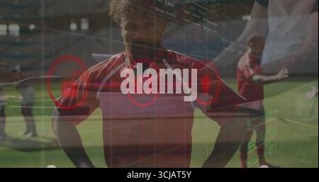 Joueur de football masculin debout portant un maillot rouge sur le terrain du stade avec superposition analytique translucide Banque D'Images