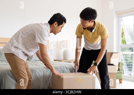 Père et fils déballant la boîte en carton ensemble dans une chambre lumineuse Banque D'Images