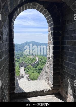 Grande muraille de Chine vue encadrée par une arche de pierre, s'étendant à travers des montagnes vertes sous un ciel bleu clair Banque D'Images