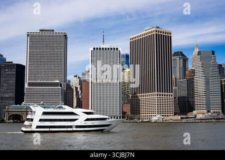 Un élégant bateau de croisière Zephyr blanc glisse sur l'eau devant l'emblématique horizon de Lower Manhattan à New York. L'image capture un juxtapo Banque D'Images
